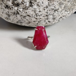 May include: A silver ring with a large, faceted, deep red gemstone. The ring is set in a simple, modern style.