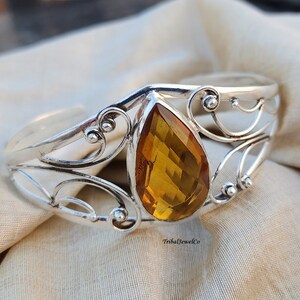 May include: A silver bangle bracelet featuring an amber gemstone at its centre. The bracelet has a delicate, ornate design.