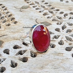 May include: A silver ring with a large, oval-shaped, red gemstone. The ring is set on a wooden surface.