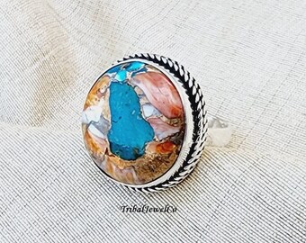 May include: A silver ring with a large, round turquoise and brown stone set in a silver bezel. The ring has a braided band.