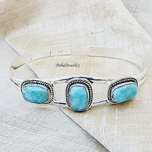 May include: A silver bangle bracelet with three rectangular turquoise stones set in silver bezels. The bracelet is open and adjustable.