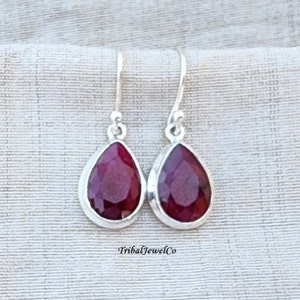May include: A pair of silver dangle earrings featuring teardrop-shaped red gemstones. The earrings have a simple design and are ideal for everyday wear.