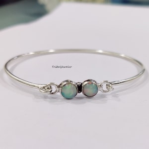 Op de afbeelding: Een zilveren armband met twee opaalstenen. De armband is simpel en elegant, de opalen hebben een mooie witte kleur met een vleugje groen.