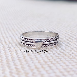 Puede incluir: Un anillo de plata con un diseño de corazón en la banda. La banda está hecha de metal retorcido en forma de cuerda.