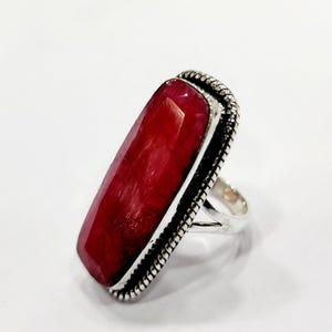 May include: A silver ring with a large, rectangular, red gemstone set in a silver bezel. The ring has a decorative, textured band.