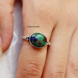May include: A silver ring with a green, blue, and brown oval gemstone. The ring has small silver beads on the band.