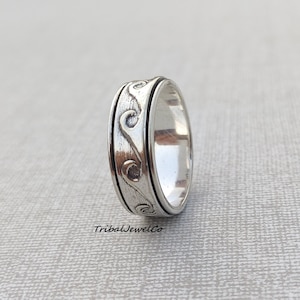 May include: A silver-colored ring with a wave-like pattern etched around the band. The ring has a textured design and a smooth, polished interior. The ring is a piece of jewelry.