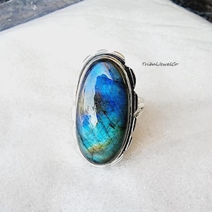 May include: A silver ring with a large oval-shaped blue labradorite gemstone. The ring has a textured band and is set in a silver bezel.