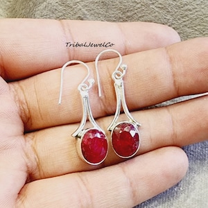 May include: A pair of silver dangle earrings with oval-shaped red ruby gemstones. The earrings have a simple, elegant design.
