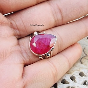 May include: A teardrop-shaped ruby ring set in sterling silver. The ring features a delicate, intricate design with multiple bands.
