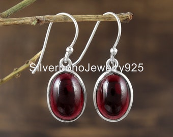 May include: A pair of silver dangle earrings featuring oval-shaped red gemstones. The earrings have a simple design and are ideal for everyday wear.