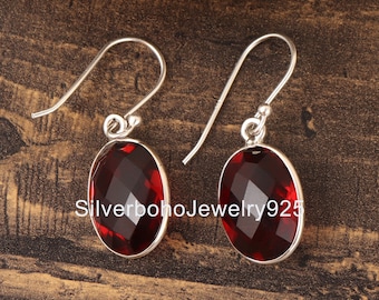 May include: A pair of silver earrings with red gemstone oval drops. The earrings have a hook fastening.