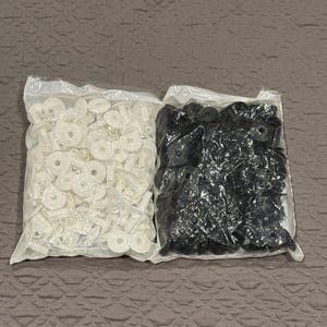 May include: Two clear plastic bags filled with automotive trim clips. One bag contains white clips, and the other contains black clips. The clips are made of plastic and are various shapes and sizes.