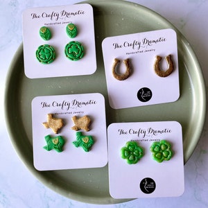 May include: Four sets of handmade polymer clay earrings on white cards with the text "The Crafty Dramatic" and "Handcrafted Jewelry". The earrings are green shamrocks, gold horseshoes, green shamrocks with gold hearts, and green Texas outlines with gold flowers.