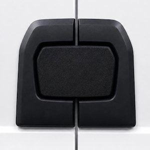 May include: A matte black, rectangular door handle with rounded corners, featuring a central push-button mechanism. The handle is mounted across the vertical seam of two white, flat-panel doors, creating a symmetrical, modern hardware look.