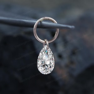 May include: A rose gold hoop earring with a clear, pear-shaped cubic zirconia pendant. The earring is displayed against a dark, textured backdrop. The focus is on the sparkling gemstone, suggesting it's designed for formal wear or special events. The earring is likely for a special occasion.