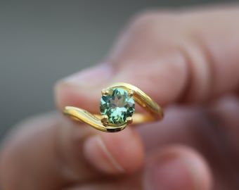 May include: A gold ring with a green gemstone set in a curved band.