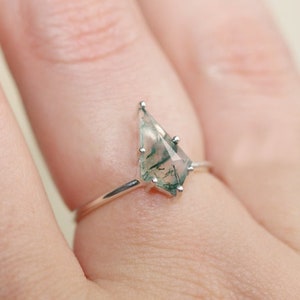 May include: A silver ring with a green and white moss agate gemstone in a unique, geometric shape.