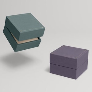 May include: Two square gift boxes, one teal and one purple, with a subtle textured finish. Both boxes have a gold trim around the top edge.