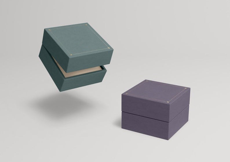 May include: Two square gift boxes, one teal and one purple, with a subtle textured finish. Both boxes have a gold trim around the top edge.