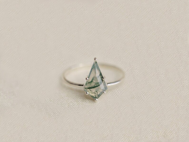 May include: A silver ring with a green agate gemstone in a faceted, kite-shaped setting.