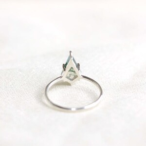 May include: A silver ring with a green gemstone set in a geometric design.