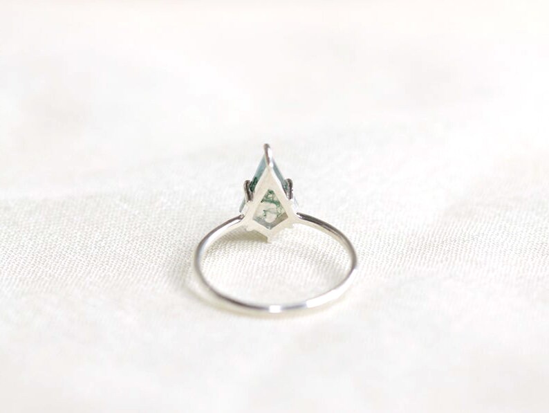 May include: A silver ring with a green gemstone set in a geometric design.
