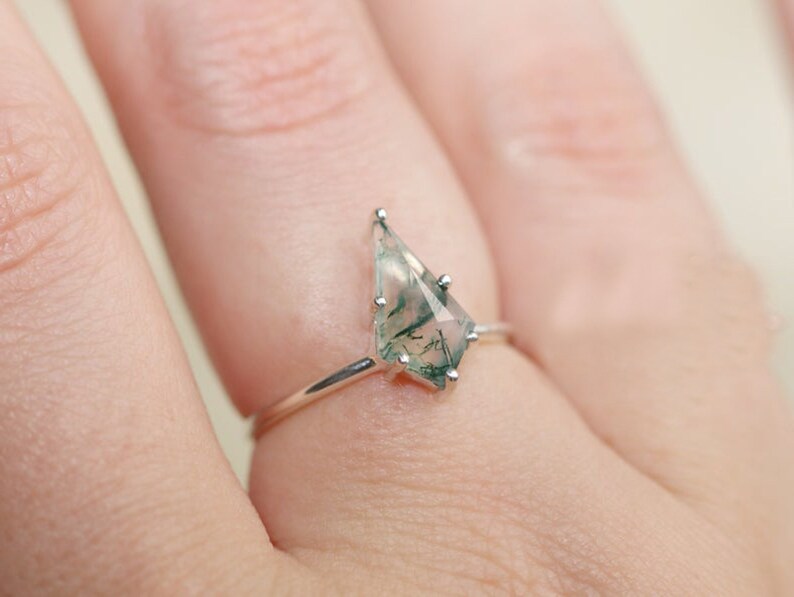 May include: A silver ring with a green and white moss agate gemstone in a unique, geometric shape.