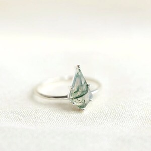 May include: A silver ring with a green and white moss agate gemstone in a teardrop shape.