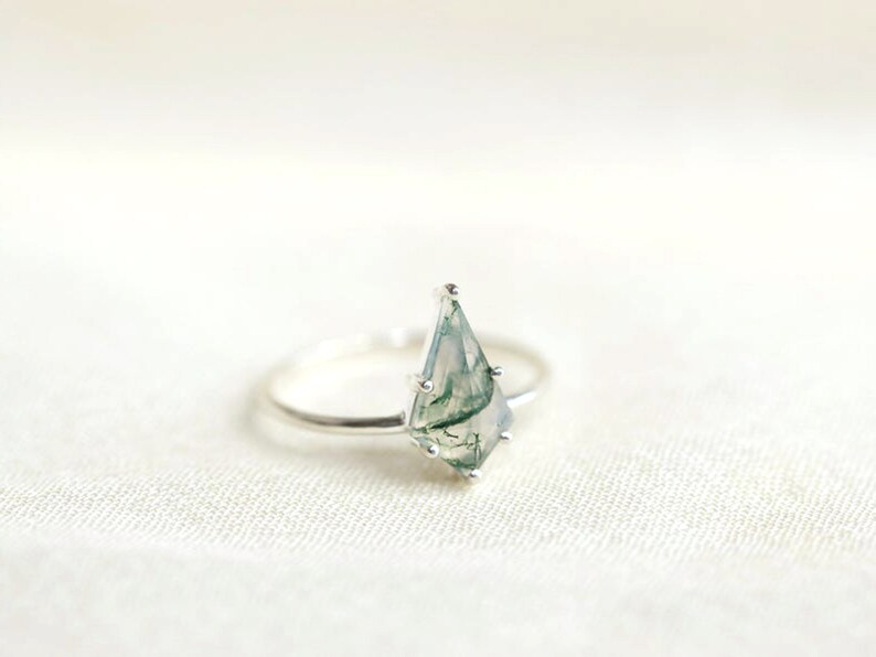 May include: A silver ring with a green and white moss agate gemstone in a teardrop shape.