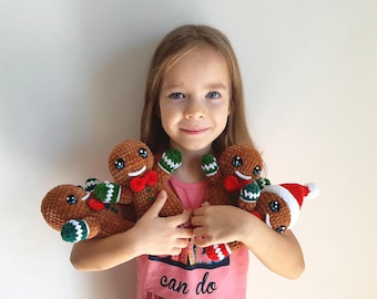 May include: A young person holding four crocheted gingerbread people toys. The gingerbread people are brown with white eyes, red mouths, and green and white striped arms. One gingerbread person is wearing a red Santa hat.