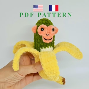 Pode incluir: Um macaco de crochê feito à mão saindo de uma casca de banana amarela. O macaco tem um corpo verde, rosto e orelhas cor de pêssego e olhos pretos. A casca da banana é de cor amarelo brilhante. O texto "PDF PATTERN" é exibido acima do macaco.