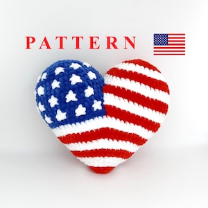 Może przedstawiać: Poduszka w kształcie serca na szydełku z wzorem amerykańskiej flagi. Poduszka jest wykonana z czerwonej, białej i niebieskiej przędzy.