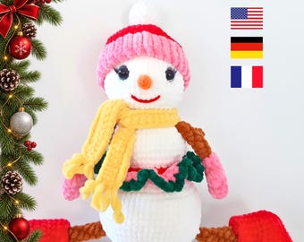 May include: A white crocheted snowman plush toy wearing a pink hat, a yellow scarf, and a dark green ruffled skirt. The snowman has brown arms, red mittens, and red boots. The text PDF PATTERN is at the top with American, German, and French flags.