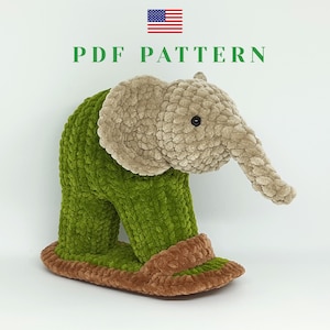 May include: A plush elephant-shaped slipper in green and tan. The elephant has a tan head and trunk, with a green body and brown trim around the foot. The text "PDF PATTERN" is above the slipper, with an American flag in the top left corner.