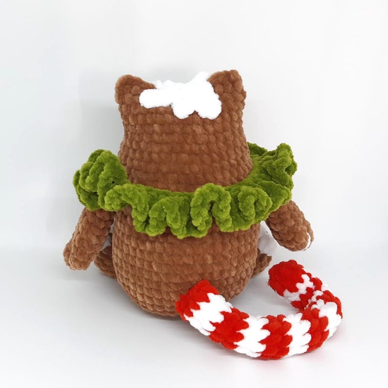 May include: A handmade brown crochet owl with a green ruffled collar and white accents. A red and white striped crochet candy cane lies nearby. The owl is a soft, plush toy.