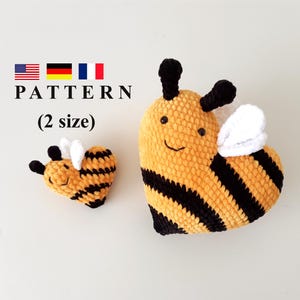 May include: Two crocheted bee plushies, one large and one small. The larger bee is heart-shaped with black and yellow stripes and white wings. The smaller bee is lying on its side with black and yellow stripes and white wings.