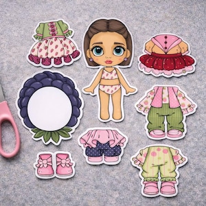 以下が含まれることがあります： 人形の切り抜きコレクション。人形のフィギュア、さまざまな衣装、アクセサリーが含まれています。衣装は水玉模様、花柄、フリルが特徴です。ピンクのはさみも含まれています。