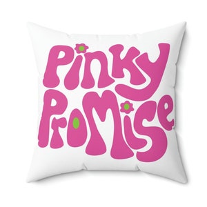Op de afbeelding: Een wit vierkant kussen met de woorden "Pinky Promise" in roze, gestileerde letters met groene bloemenaccenten.
