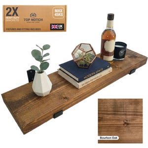 A Bourbon Oak Stain dark brown wooden shelf with black brackets, holding decorative items like a geometric terrarium, books, a candle, and a bottle. The shelf is made of Bourbon Oak. The image also shows a box with the text "2X HEAVY DUTY BRACKETS".