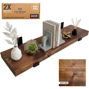 Dark oak floating shelf with black brackets, holding books, decorative items, and a small terrarium. The shelf is made of wood and includes a box of heavy-duty brackets. The shelf can hold up to 45 kg.