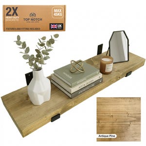 A wooden floating shelf in antique pine, supported by black brackets. It displays a white vase with foliage, books, a candle, and a mirror. The shelf is rated for a maximum weight of 45 kg.