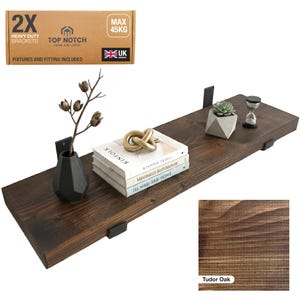 A Tudor Oak wooden shelf with black brackets, holding decorative items. The shelf supports a stack of books, a gold knot sculpture, a small succulent in a geometric pot, and an hourglass. Includes "2X Heavy Duty Brackets" and "Max 45KG".