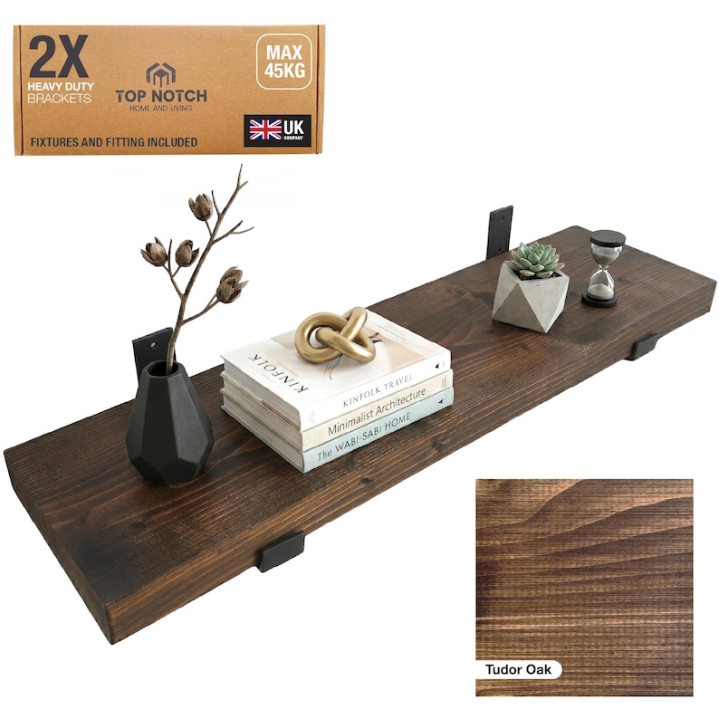 A Tudor Oak wooden shelf with black brackets, holding decorative items. The shelf supports a stack of books, a gold knot sculpture, a small succulent in a geometric pot, and an hourglass. Includes "2X Heavy Duty Brackets" and "Max 45KG".