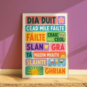 Puede incluir: Una lámina decorativa rectangular con bloques coloridos que contienen frases en irlandés como DIA DUIT, CÉAD MÍLE FÁILTE, FÁILTE, CRAIC AGUS CEOL, SLÁN, GRÁ, TÁ, MAIDIN MHAITH, SLÁINTE y GHRIAN, junto a iconos de una flor, notas musicales, corazón, sol y copas.