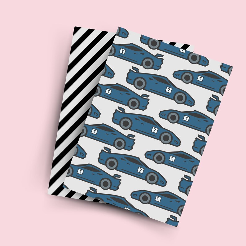 May include: A white sheet of wrapping paper with a repeating pattern of blue race cars with the number 7 on them. The cars are outlined in black and have black wheels. The paper is layered on top of a black and white striped sheet of wrapping paper.