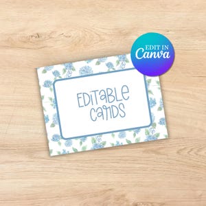 May include: Editable cards with a blue hydrangea floral pattern. The text "EDITABLE CARDS" is printed on the card. The card is on a wood surface.