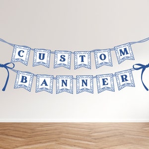 May include: A blue and white banner with the text "CUSTOM BANNER" in blue letters. The banner is strung with blue ribbon and has a blue bow on each end.
