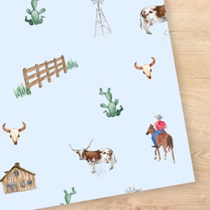 May include: A light blue background with watercolor illustrations of a ranch theme. The design includes a wooden fence, cacti, a windmill, a barn, a cow, a longhorn, a bull skull, and a cowboy on a horse.