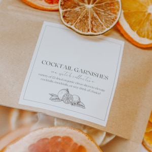 May include: A brown paper bag filled with dried citrus slices for cocktail garnishes. The bag has a white label that reads "Cocktail Garnishes - an witch collective - variety of 12 dried organic citrus slices to elevate cocktails, mocktails, or any drink of choice!"